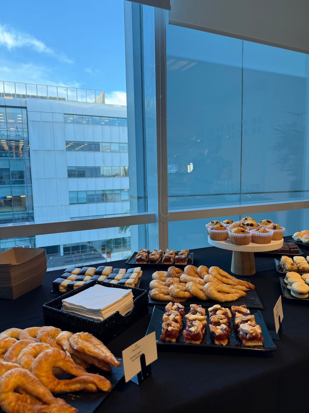 Bandejas de facturas, medialunas y pastelería sobre mesa negra en un desayuno corporativo