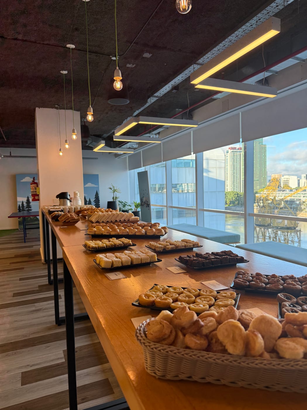 Mesa larga de desayuno con panes, facturas y medialunas frente a un ventanal con vista al río
