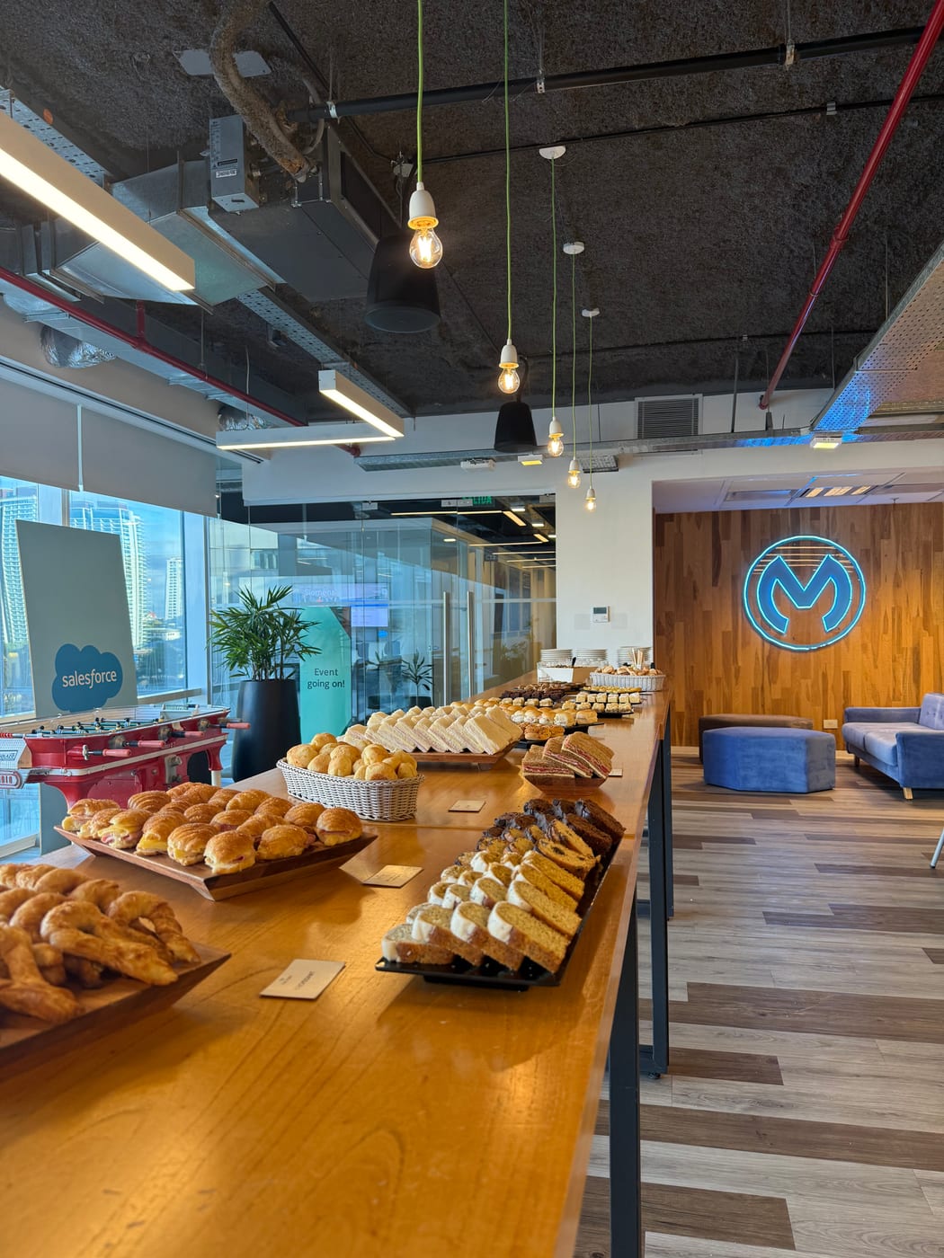 Estacion de desayuno con medialunas y facturas en bandejas dentro de una oficina corporativa