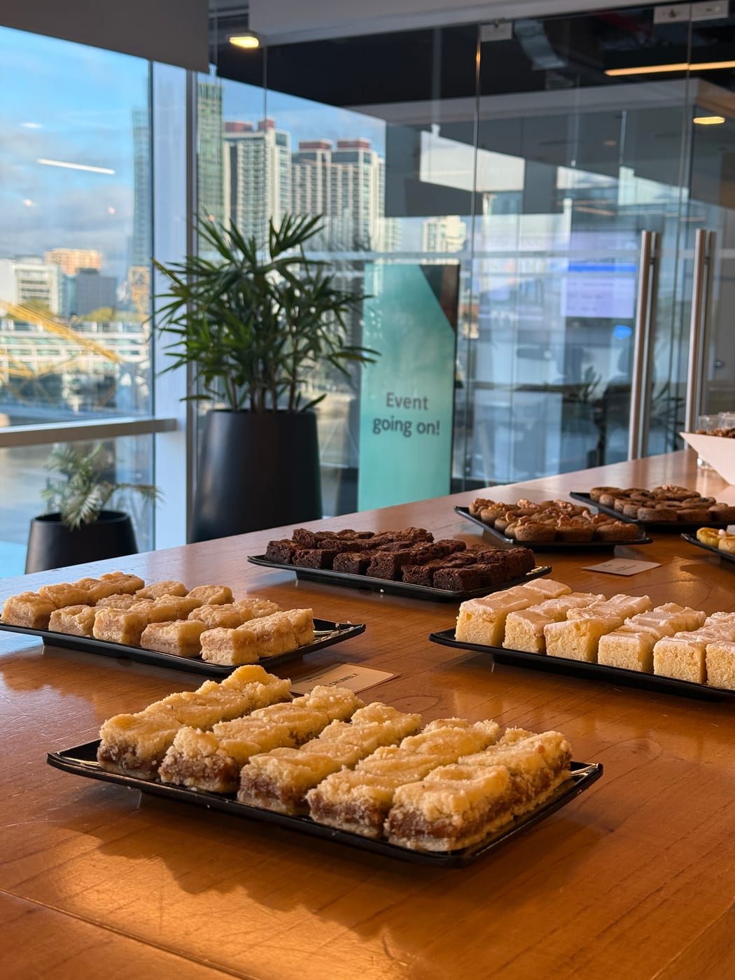 Bandejas de facturas glaseadas y budines en una mesa de coffee break junto a ventanal