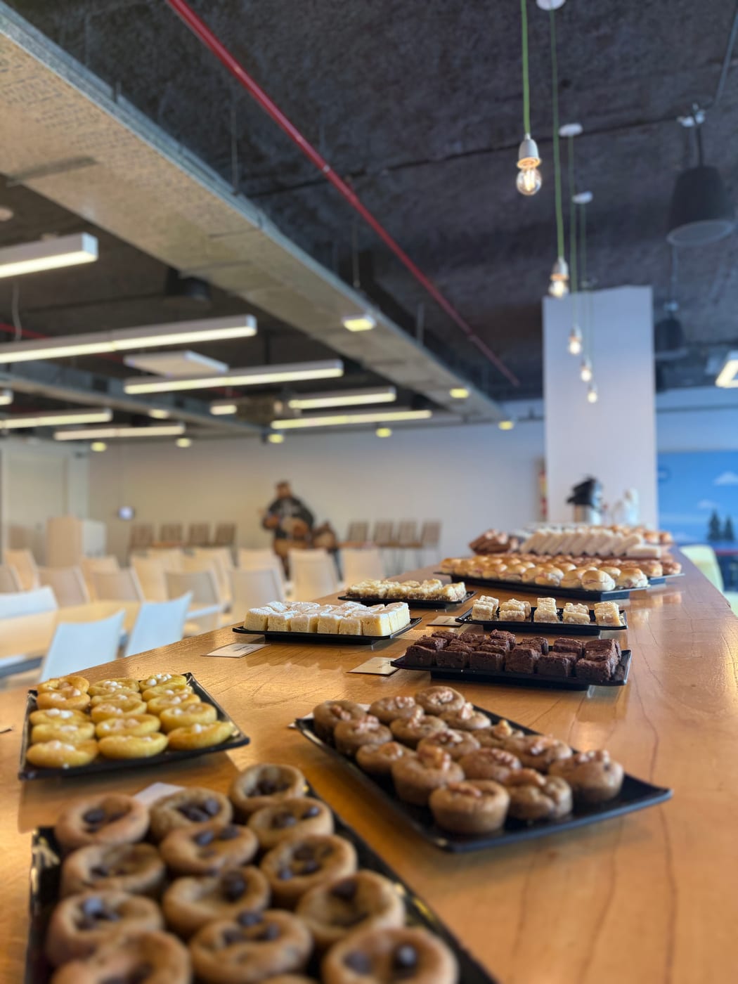 Extenso buffet de coffee break con cookies, mini pasteleria, brownies y bocados dulces sobre mesa larga