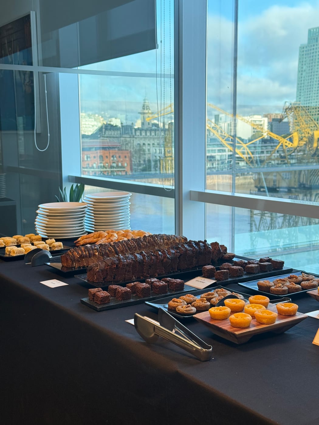Mesa de coffee break con brownies, donas y cookies junto a ventanal con vista a la ciudad