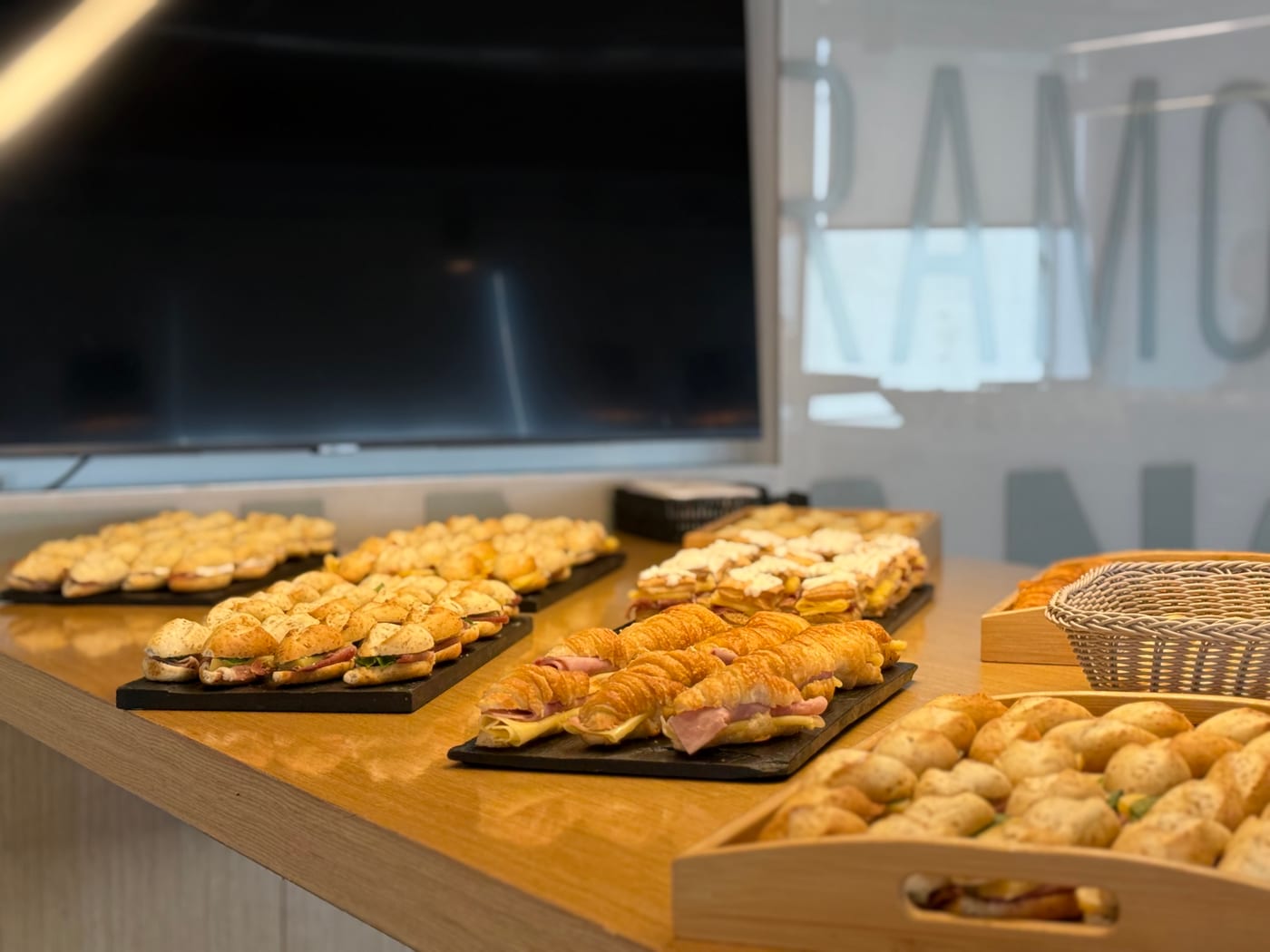Bandejas de sandwiches, medialunas de jamon y queso y pan de queso servidas para un desayuno de oficina