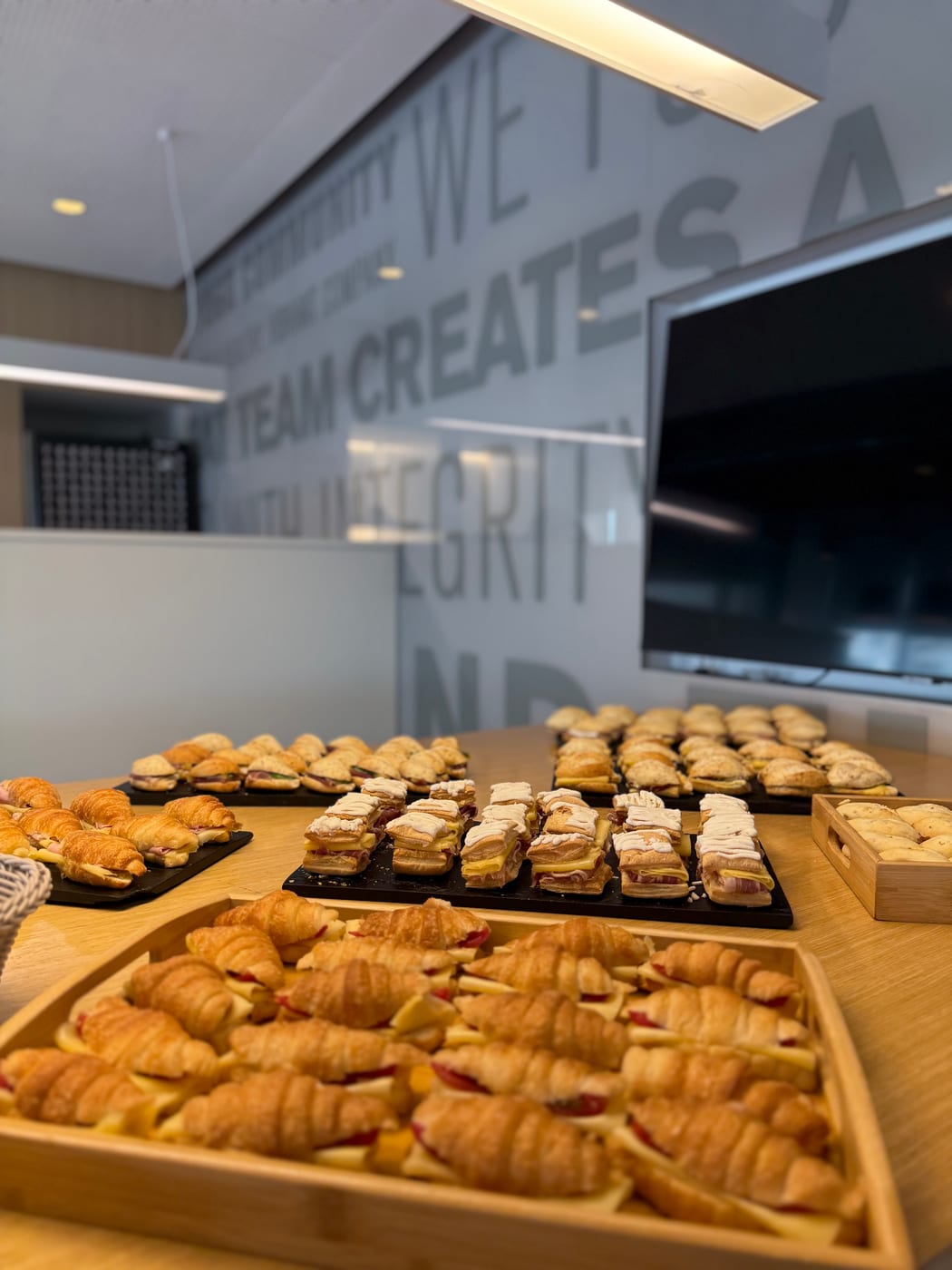 Mesa de desayuno corporativo con medialunas, sandwiches y facturas en bandejas