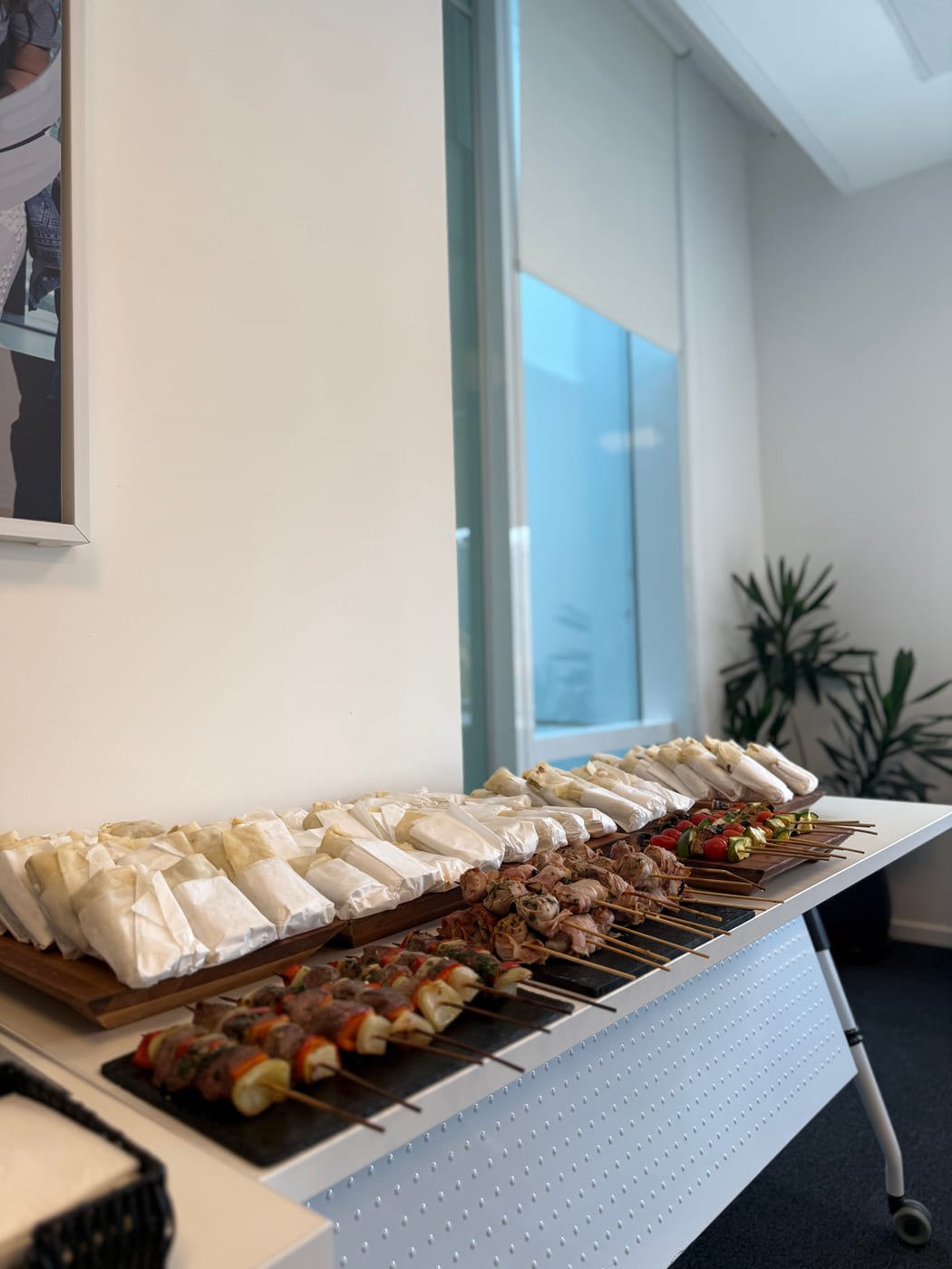 Buffet corporativo con sandwiches de miga y brochettes de carne y vegetales en oficina