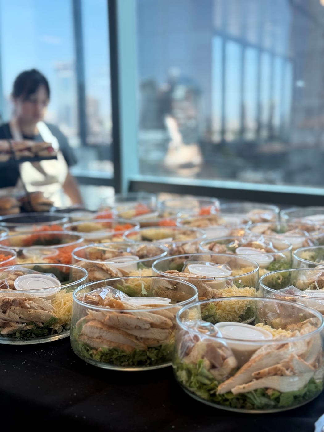 Ensaladas Caesar individuales con pollo en vasos sobre mesa de evento con vista a la ciudad