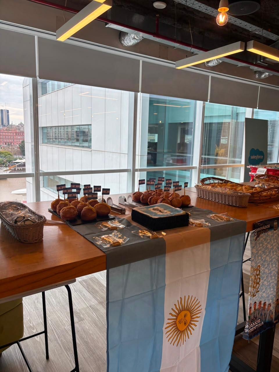 Desayuno tematico con banderas argentinas, pan y facturas junto a un ventanal
