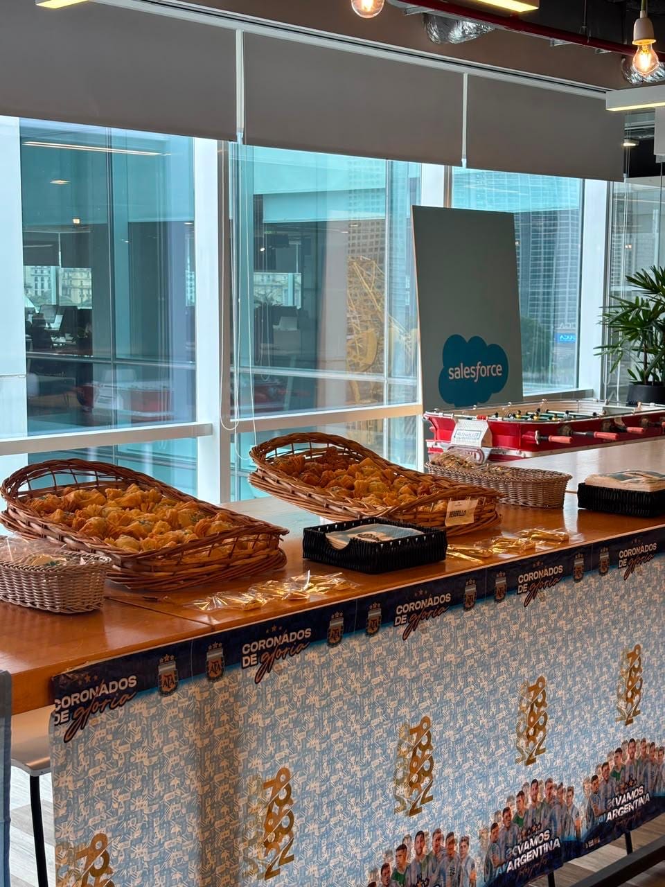Mesa de desayuno corporativo con canastas de facturas y medialunas en una oficina