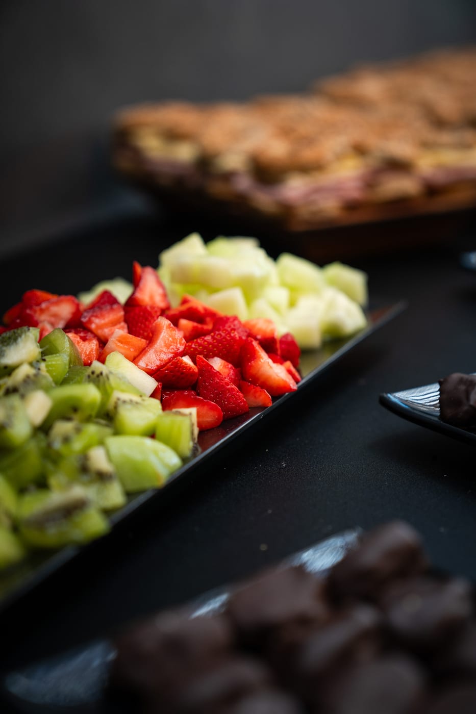 Detalle de bandeja de frutas frescas cortadas con frutilla, kiwi y melon en un desayuno corporativo