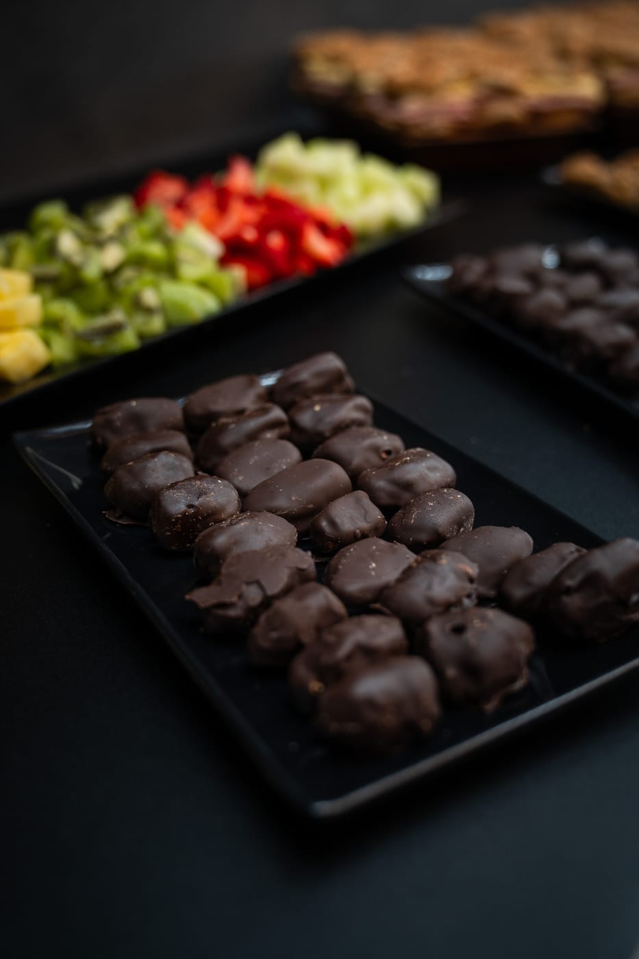 Bandeja de bombones y barritas bañadas en chocolate junto a frutas frescas para un coffee break