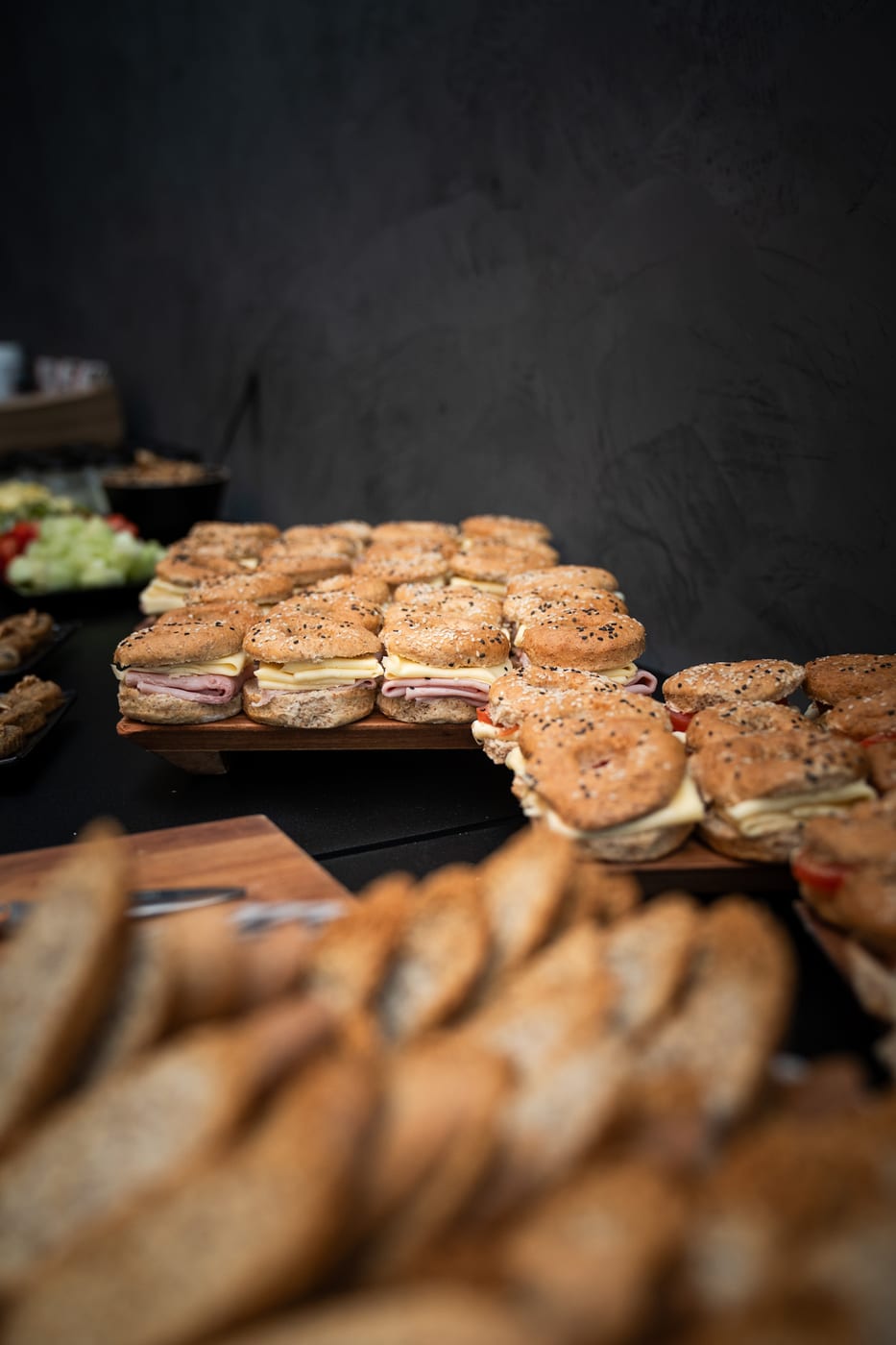 Tabla de sandwiches en pan integral con semillas rellenos de jamon y queso, junto a rodajas de pan de campo, en un buffet de catering corporativo