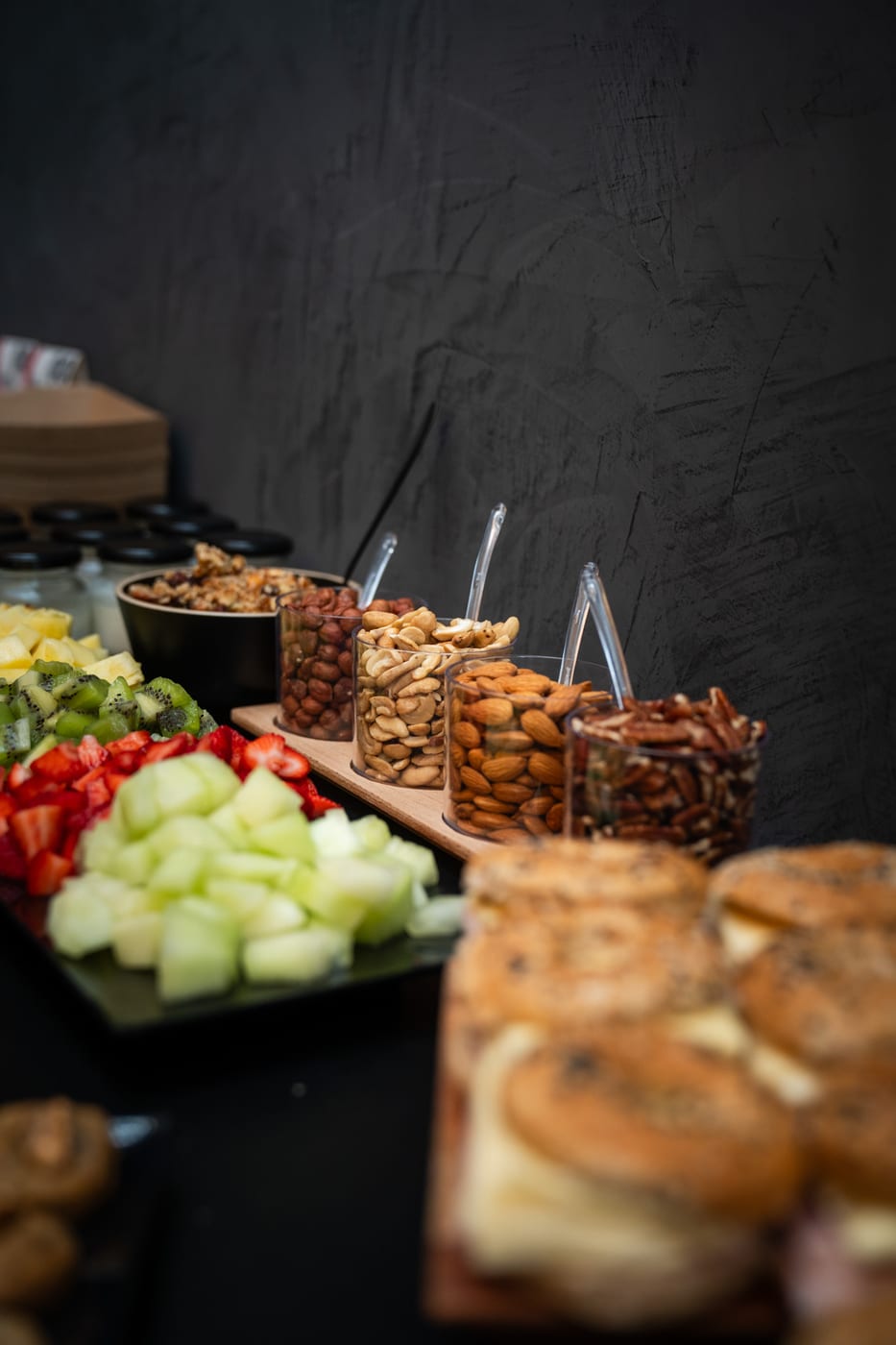 Mesa de desayuno saludable con frutas frescas cortadas (kiwi, frutilla, melon, ananá), granola y vasitos de frutos secos surtidos para un evento corporativo