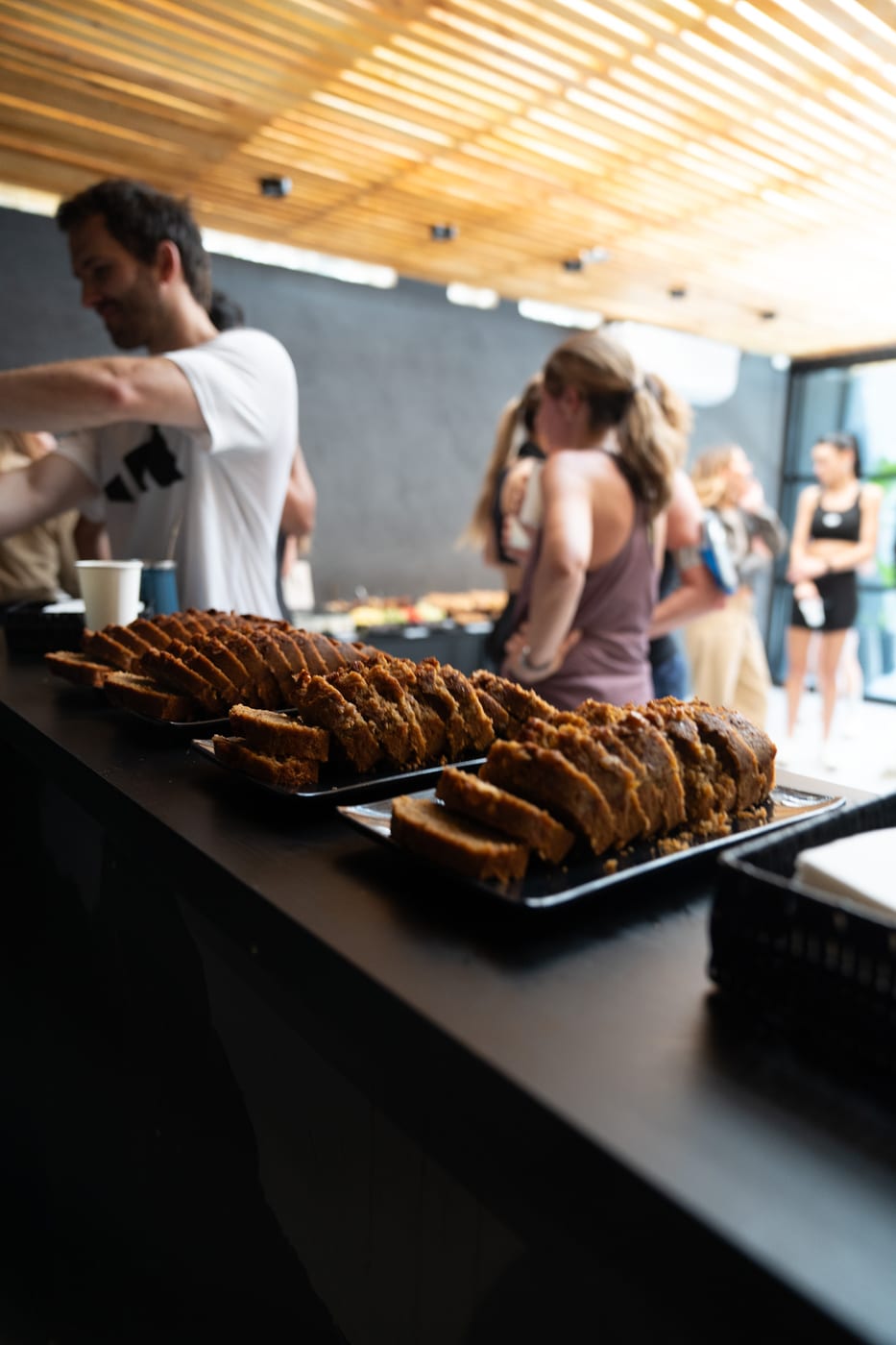 Bandejas de budin casero en rodajas servidas en un coffee break al aire libre durante un evento corporativo con invitados de fondo