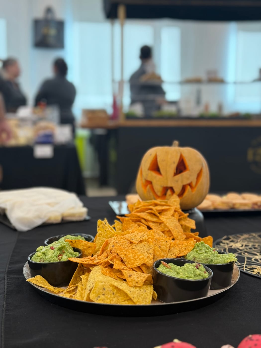 Plato de nachos con guacamole y calabaza tallada de Halloween sobre mesa negra en un evento tematico