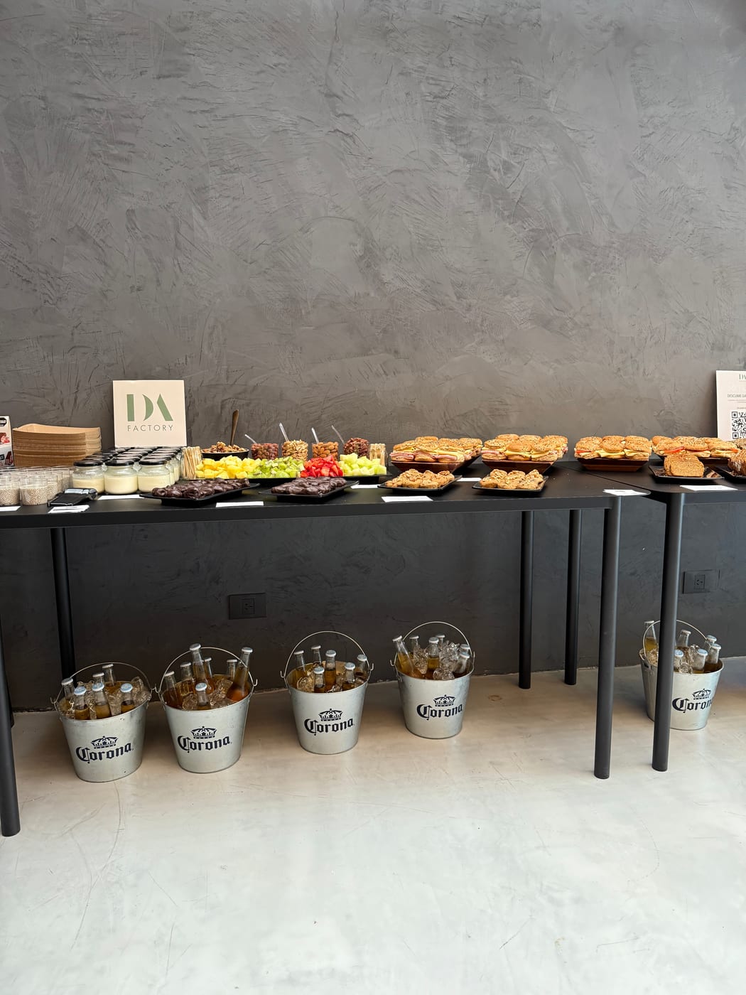 Recepcion con mesa de bocados salados y baldes de cerveza frios debajo, montaje de after office con branding de DA Catering
