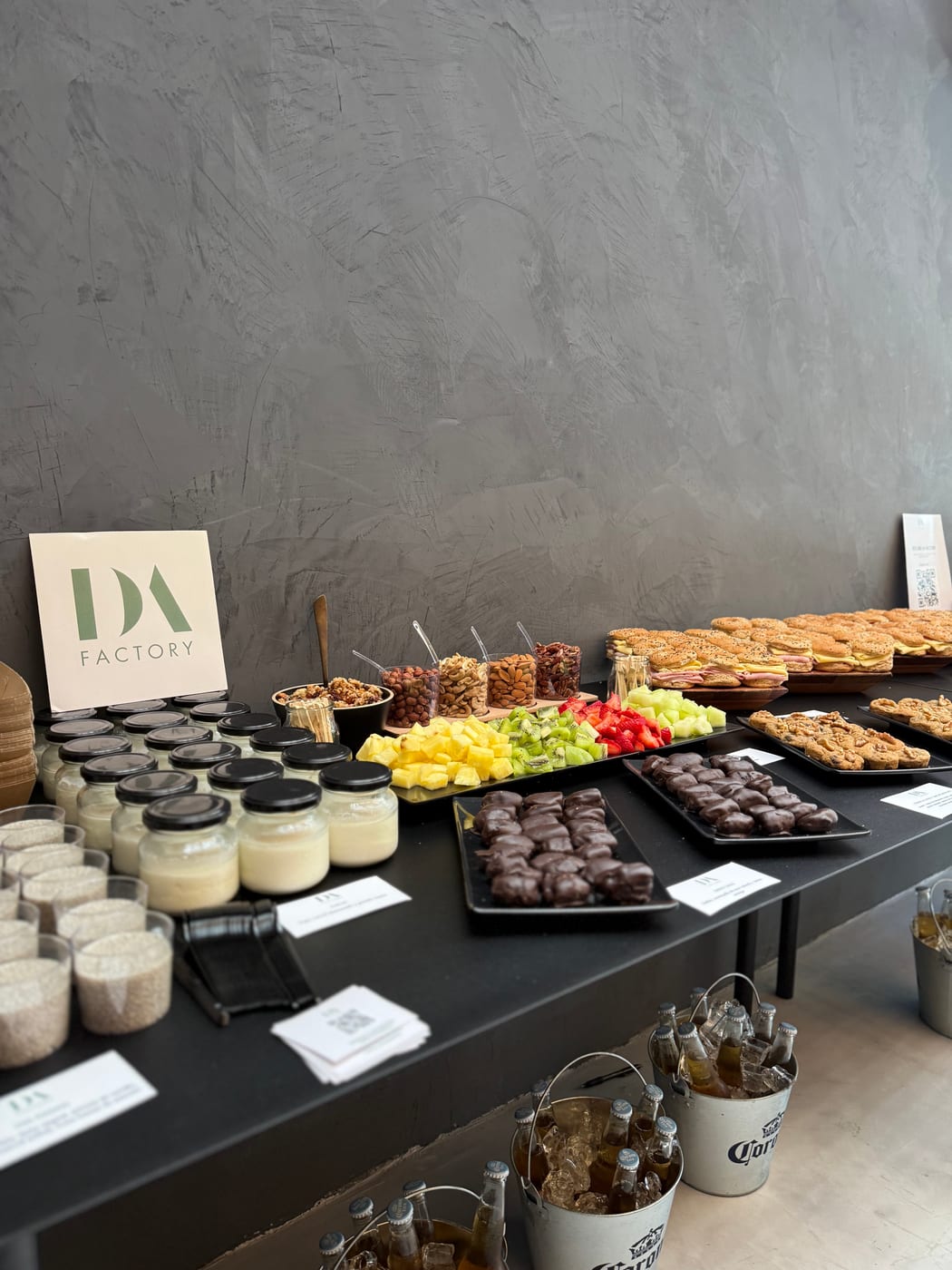 Mesa de coffee break con copas de postre, bombones de chocolate, frutos secos, brochettes dulces y panificados para un evento corporativo de DA Catering