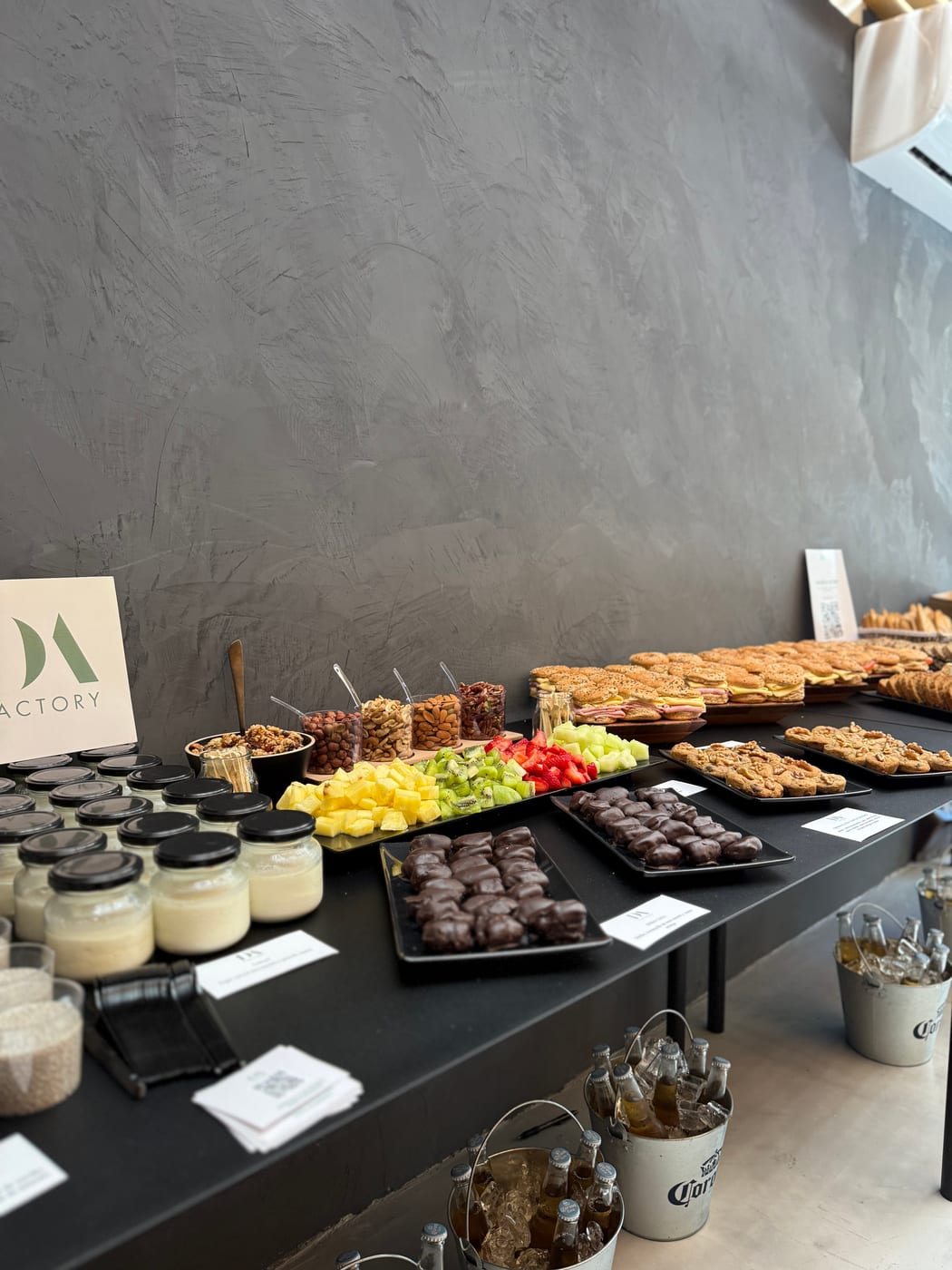 Mesa de coffee break con copas de postre, bombones de chocolate, frutos secos y brochettes dulces en un montaje corporativo de DA Catering