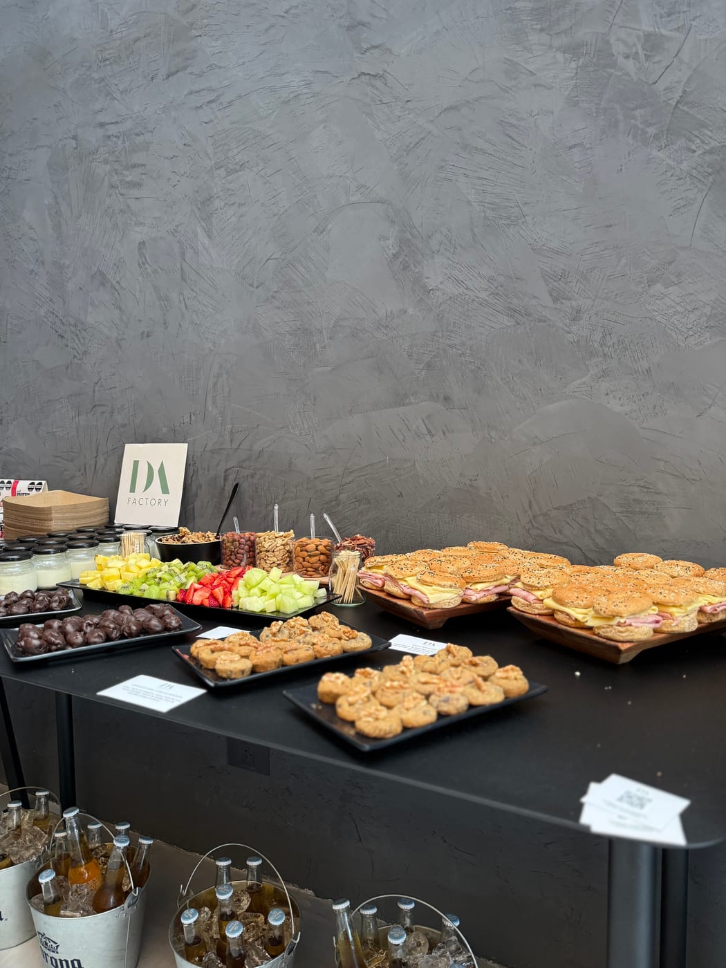 Buffet de almuerzo con mini sandwiches de jamon y queso en pan con semillas, scones salados y tabla de frutas y encurtidos para un evento corporativo de DA Catering