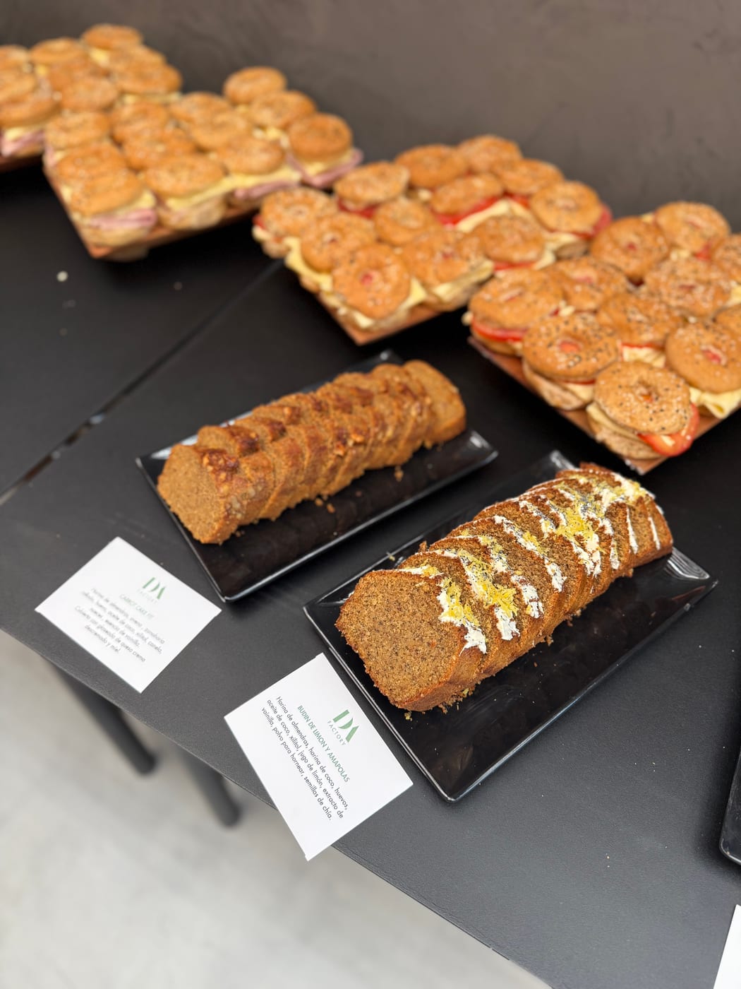 Budines en rodajas glaseados y bandejas de mini sandwiches en un montaje de coffee break de DA Catering