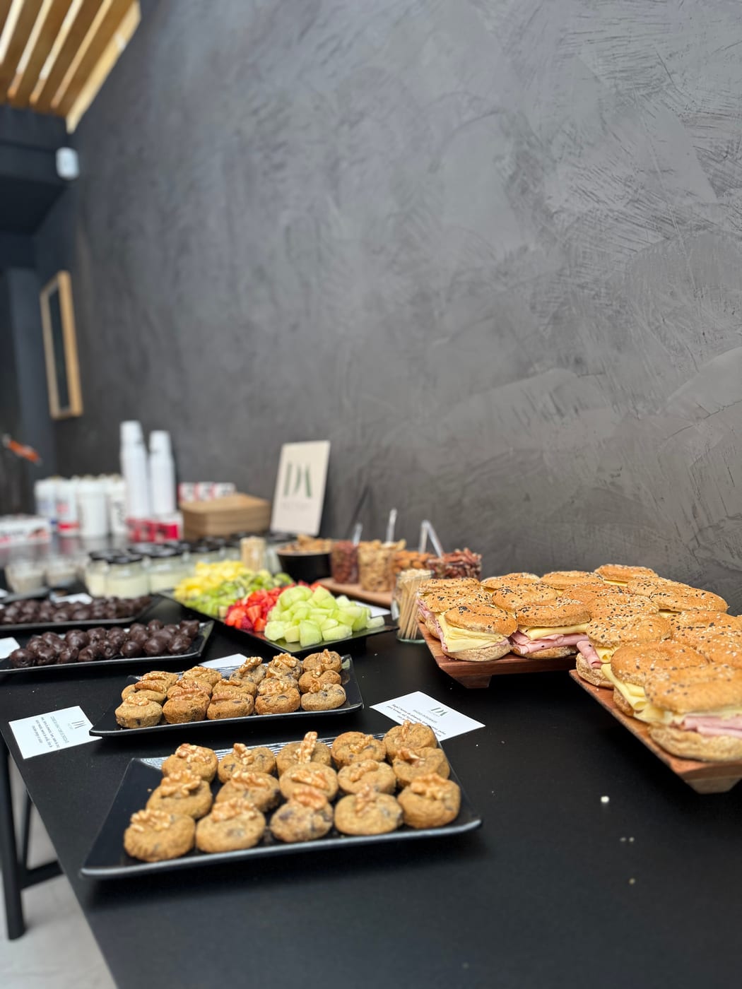 Buffet de almuerzo con sandwiches de jamon y queso en pan con semillas, scones salados y tabla de frutas y verduras para un evento corporativo de DA Catering