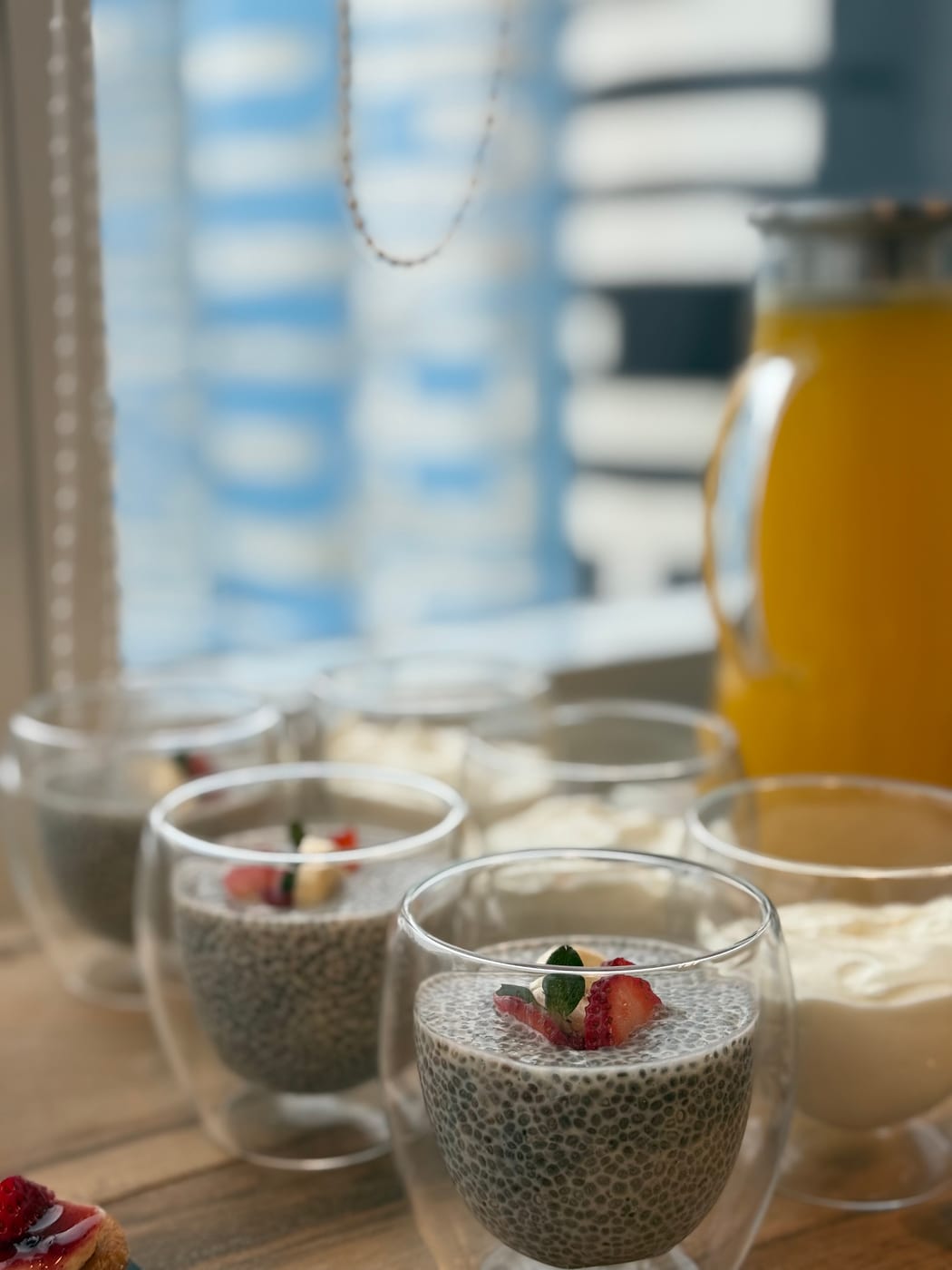 Vasos de pudding de chia con frutillas y menta junto a jugo de naranja y crema, servicio de desayuno saludable junto al ventanal
