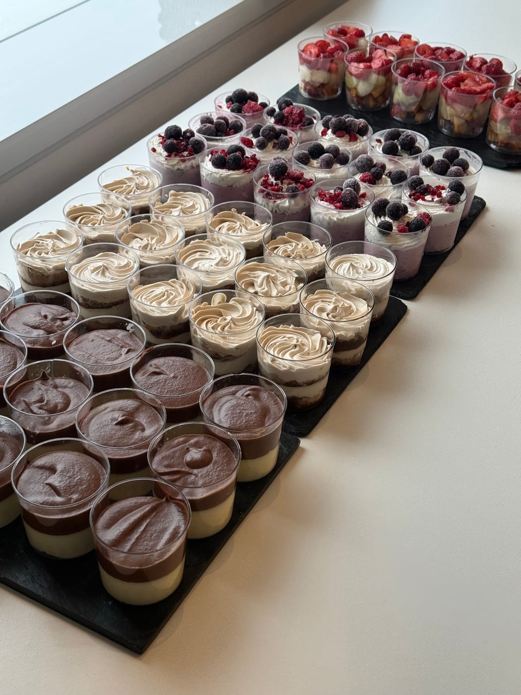 Mesa dulce con copas individuales de postre: chocolate, crema con merengue y frutos rojos con crema, dispuestas en bandejas negras
