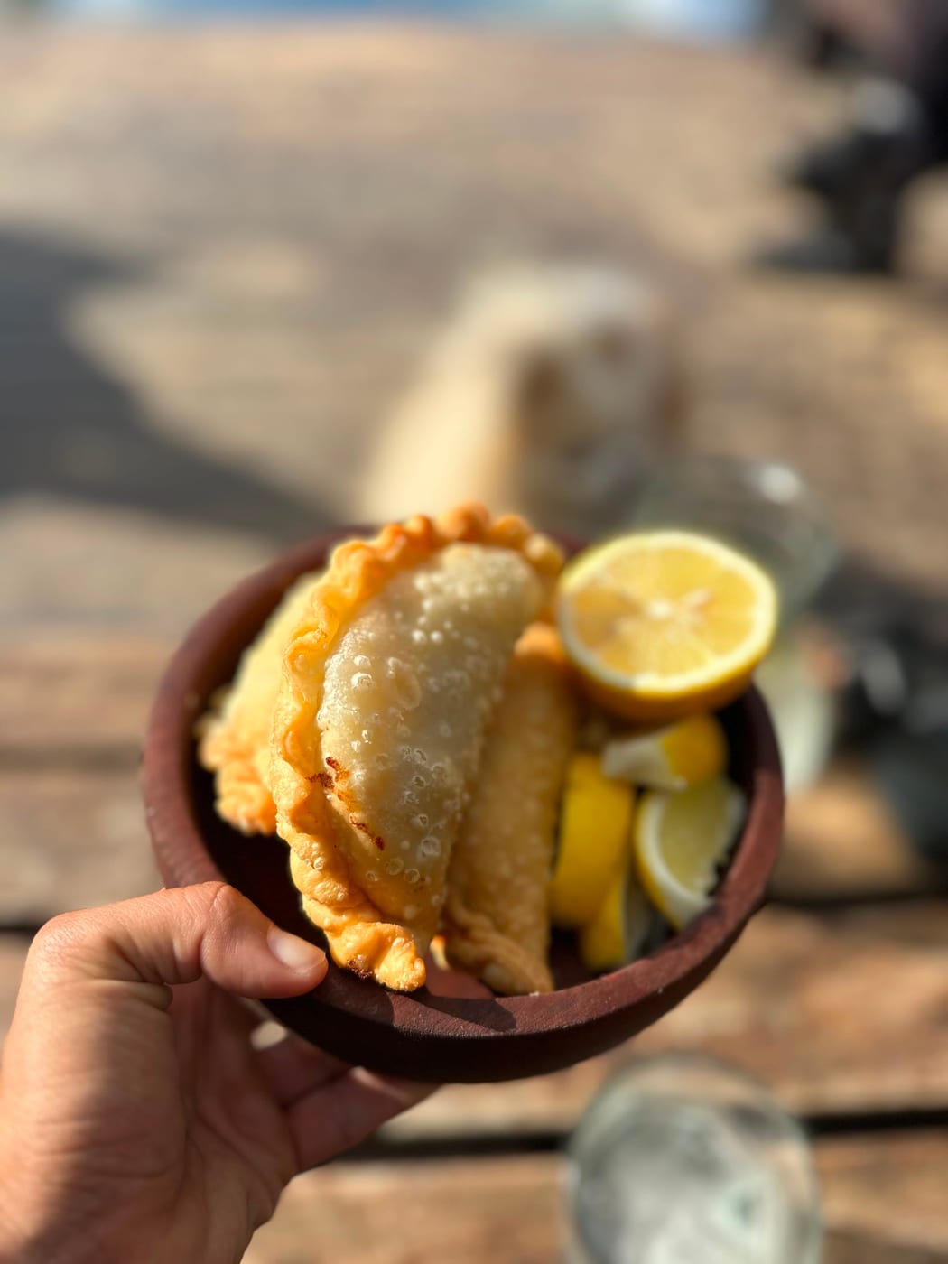 Empanadas fritas recien hechas servidas en cuenco de barro con gajos de limon, en un evento al aire libre